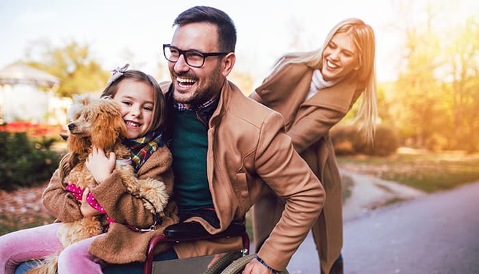 Disabled father in wheelchair enjoying the outdoors with his daughter and wife in an autumn park